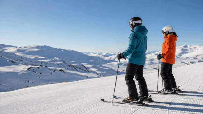 Dos esquiadores equipados en una pista de nieve con vistas a la montaña