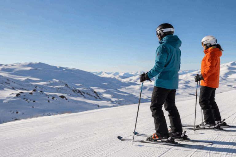 Dos esquiadores equipados en una pista de nieve con vistas a la montaña